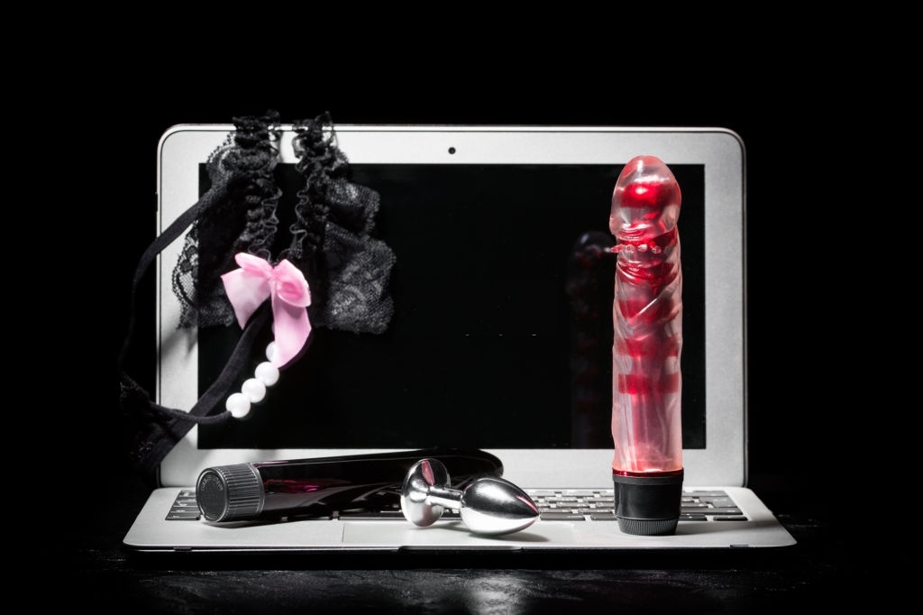 Adult webcam and virtual sex chat concept. Laptop with female panties, dildo vibrator and buttplug on black background